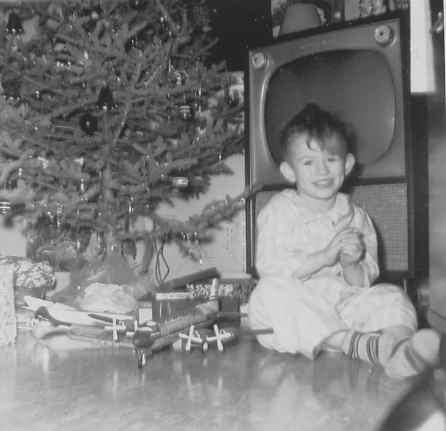 Not absolutely sure of the date on this one, but it's probably Christmas 1959. I was born in August 1956 which would make me three and a bit when the picture was taken, which seems about right. The picture was taken by my Grandfather with a Kodak Brownie Hawkeye (with flash and leather case), which I still have. The airplane, which was my proudest present that year is a tin-plate DC-7 in United Airlines colours. It has a clear plastic bit over the passenger compartment and a friction motor that spins the props when you push the plane along the floor. The  wing assembly detaches, probably because that was the only way they could make the plane. If you had skinny fingers (which I do) when you took the wings off you could stick the tip of your finger through the open door at the back of the passenger compartment. I still have the plane, though it's not in pristine condition. A couple of years after this photo was take I noticed on TV that when the propellers of real airplanes spun you didn't see the tips and on my plane you did - out came the scissors and off came the tips. I still have the plane and the camera, and all too few of the glass ornaments on that tree. The socks (thankfully) are gone forever, although they and the TV are immortalized in my blog profile photo.